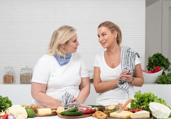 Two women in a kitchen preparing fresh vegetables and cheese with olive oil and spices.