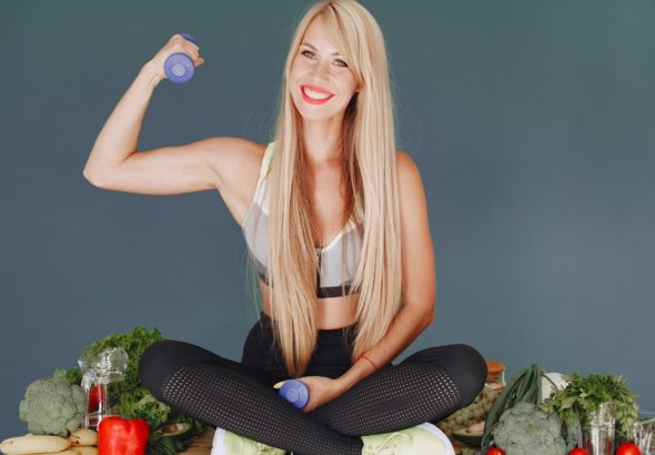 Woman lifting a small dumbbell while surrounded by fresh vegetables, embodying health and fitness.